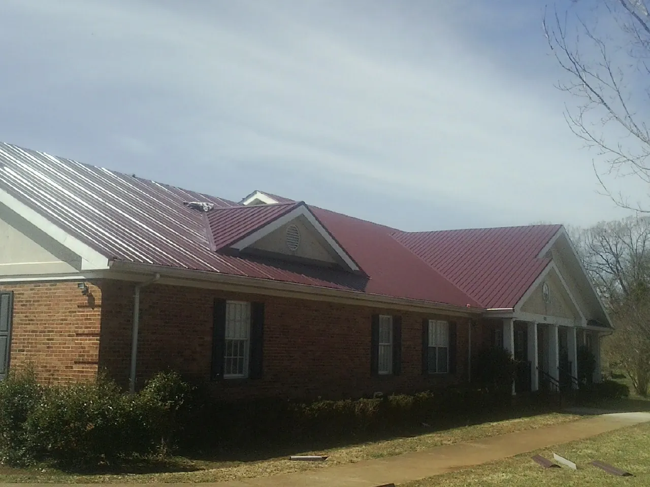 Red metal roof with gabled entries on a long brick building, from a Hail Damage Roof Repair job in Arona