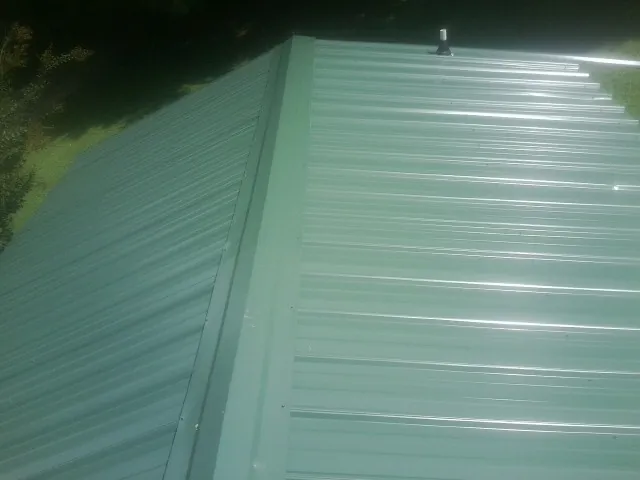 New green metal panels meeting at the ridge of a roof — Flat Roof Repair work by our crew in Arona