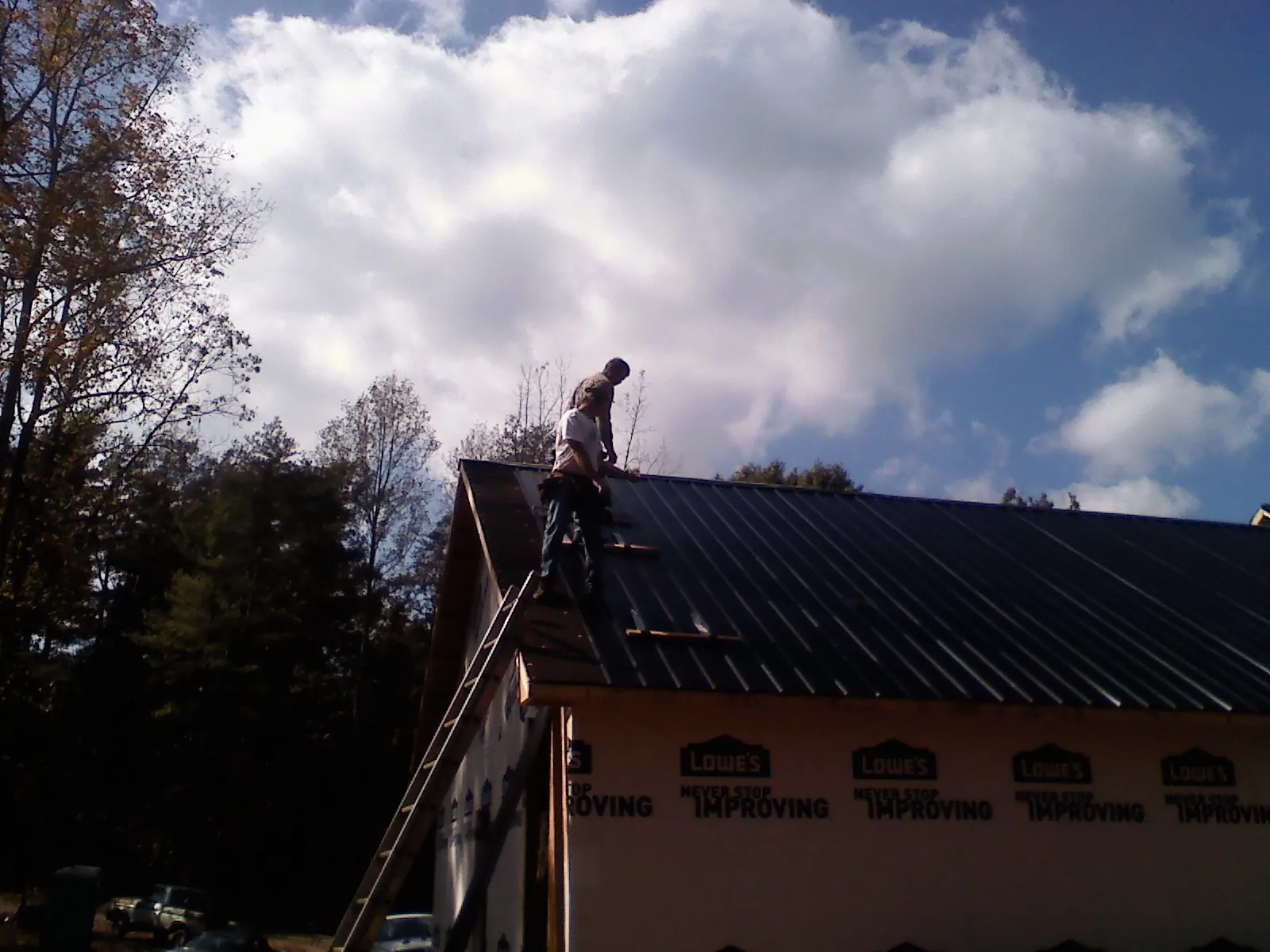 Roofer fastening dark metal panels high against a cloudy sky, from a Roof Inspection job in Arona