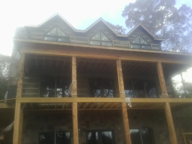 Dormers and porch framing on a large log home under construction — Roof Coating work by our crew in Arona
