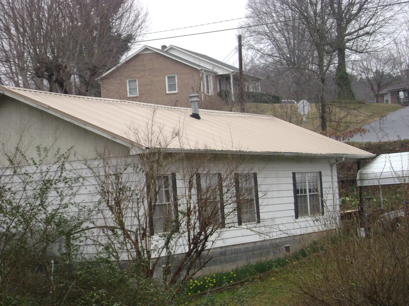 Tan metal roof on a white sided house set into a hillside — Commercial Roofing by Roofing Brothers in Arona