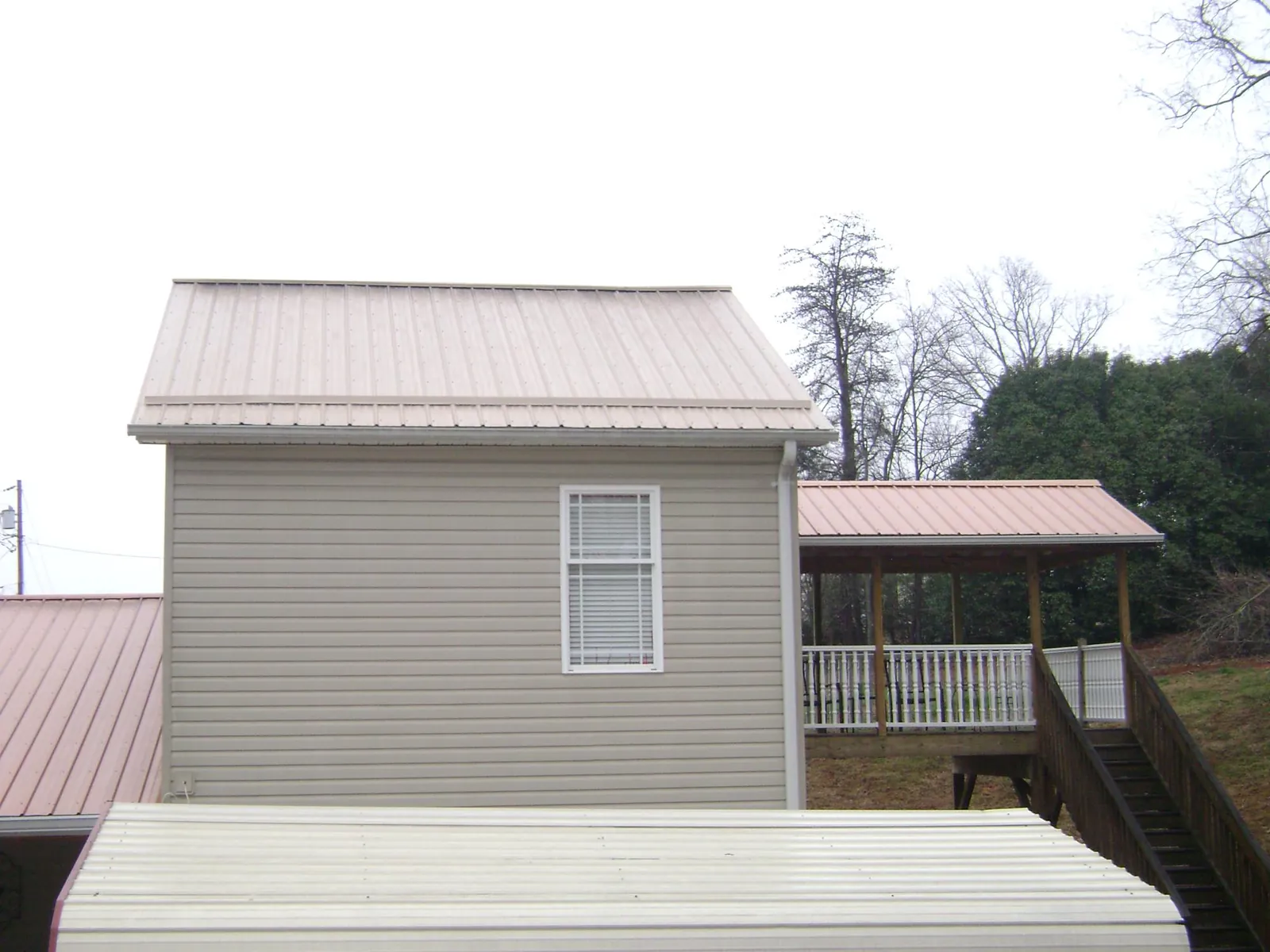 Tan metal roofs on a two story addition and attached porch, from a Roof Replacement job in Arona